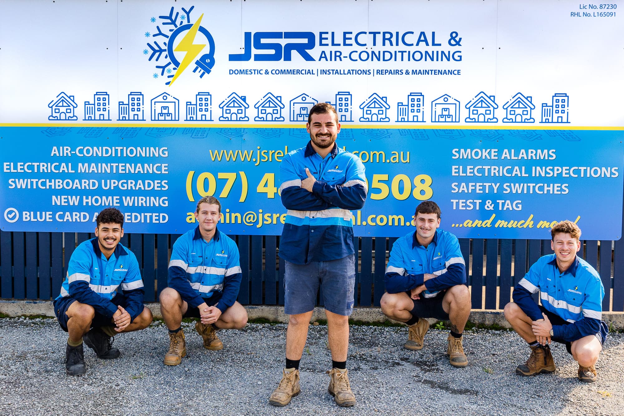 Staff members in Mackay posing and smiling in front of a sign advertising electrical services.
